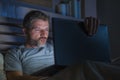 Man alone in bed playing cybersex using laptop computer watching sex movie late at night with lascivious pervert face Royalty Free Stock Photo