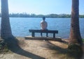 Man alone sitting on Bench in front of lake under the sun and palm tree -image Royalty Free Stock Photo