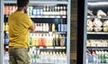 Man alone and  at the supermarket or minimarket choosing his drink or snack in big fridge with lots of products - Royalty Free Stock Photo