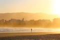 A man alone walking on the beach sand at dusk. Golden sunset light over the entire environment