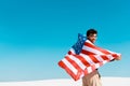Man with american flag on windy sandy beach against clear blue sky