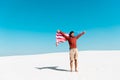 Man with american flag on windy sandy beach against clear blue sky