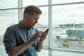 Man in anxious looks at the phone standing near window at the airport