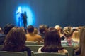 Man appears on stage in theater with many people