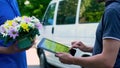 Man appending signature on tablet and receiving flower present from delivery man