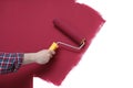 Man applying burgundy paint with roller brush on white wall, closeup Royalty Free Stock Photo
