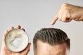 Man applying a clay, pomade, wax, gel or mousse from round metal box for styling his hair after barbershop hair cut