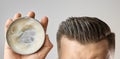 Man applying a clay, pomade, wax, gel or mousse from round metal box for styling his hair after barbershop hair cut