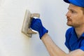 man applying decorative facade plaster with trowel on house exterior