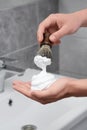 Man applying shaving foam onto brush in bathroom, closeup Royalty Free Stock Photo