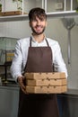 Man in apron holding pizza boxes operates in pizza cafe managing express service and takeaway orders