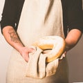 A men in an apron holds various fresh bread loaves with golden crisp in her hands. Homemade alternative bread