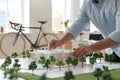 Man arranges trees on architectural model, modern office setting with bicycle