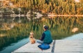 Man as a dog owner and his friend beagle dog are sitting on the wooden pier on the mountain lake and enjoying the landscape during