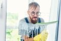 Man as a professional cleaner in blue uniform washing window with rubber brush indoors Royalty Free Stock Photo