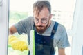 Man as a professional cleaner in blue uniform washing window with rubber brush indoors Royalty Free Stock Photo