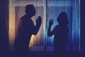 A man asks a woman for forgiveness. Silhouette of husband and wife couple at night window, domestic quarrel concept