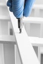 Man assembling a white flat pack ladder shelving unit with a screwdriver.