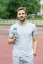 Man with athletic appearance holds bottle with water. Athlete drink water after training at stadium on sunny day. Man Royalty Free Stock Photo