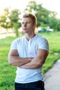 The man atlen stands in the park with headphones, a white T-shirt. Summer lifestyle, motivation is strong. Muscular arms