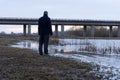 A man back to camera, standing by a lake in the countryside in winter