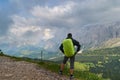 Man with backpack and green rain cover looking at the stormy clouds towards a valley bellow Sella mountains in the Dolomites