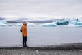 Man with a backpack standing on the beach against the background of an glacier lagoon with icebergs and views of the snow-capped