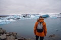 Man with a backpack standing on the beach against the background of an glacier lagoon with icebergs and views of the snow-capped