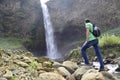 A man with a backpack is standing in front of a waterfall in Banos de Agua Santa, Cascada Manto de la Novia. Banos