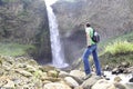 A man with a backpack is standing in front of a waterfall in Banos de Agua Santa, Cascada Manto de la Novia. Banos