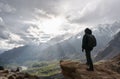A man with backpack standing on mountain peak and bright sunlight through cloudy sky. Travel lifestyle and achievement success con Royalty Free Stock Photo
