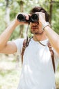 Man with backpack standing and using binoculars in forest Royalty Free Stock Photo