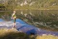 A man with a backpack stands against the backdrop of a mountain lake with a reflected sky, mountain and clouds Royalty Free Stock Photo