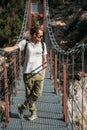 A man with a backpack on a suspension bridge against the backdrop of a mountain landscape with trees. Hiking trail pass