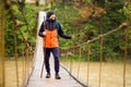 Man with backpack trekking in forest by hinged bridge over river. Cold weathe. Spring hiking. Wooden bridge across the river Royalty Free Stock Photo