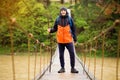 Man with backpack trekking in forest by hinged bridge over river. Cold weathe. Spring hiking. Wooden bridge across the river Royalty Free Stock Photo