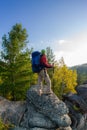 Man with backpack and trekking pole in bandana standing on a rock at dawn on a background autumn forest