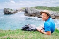 Man backpacker traveler rests on the rocky sea side, looks in ca