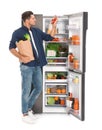 Man with bag of groceries and tomatoes near open refrigerator on background
