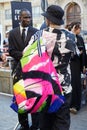 Man with bag in pink, black and blue colors and shirt with crane birds design before Palm Angels