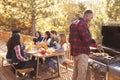 Man barbecues for friends at a table, on a deck in a forest