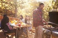 Man barbecues for friends at a table on a deck in a forest