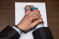 A man with bare hands in handcuffs sits at a table in front of a blank sheet of paper and a fountain pen. Concept: the detainee