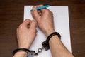 A man with bare hands in handcuffs sits at a table in front of a blank sheet of paper and a fountain pen. 7 Royalty Free Stock Photo