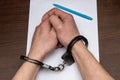 A man with bare hands in handcuffs sits at a table in front of a blank sheet of paper and a fountain pen. 3 Royalty Free Stock Photo