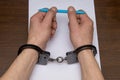 A man with bare hands in handcuffs sits at a table in front of a blank sheet of paper and a fountain pen. 5