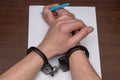 A man with bare hands in handcuffs sits at a table in front of a blank sheet of paper and a fountain pen. 6 Royalty Free Stock Photo