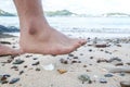 Man barefoot walking on the beach, with risk to step on piece of glass, concept of dangerous waste on the beach