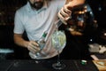 Man bartender makes a delicious cocktail with the addition of white wine, ice cubes and apple slices on a dark background