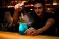 man bartender skillfully sprinkles on glass of blue cocktail decorated with mint and red raspberries.